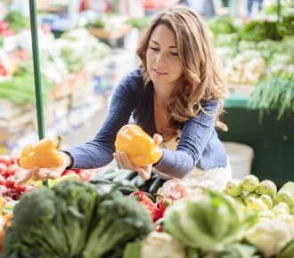 Young woman choosing between two yellow peppers at the supermarket